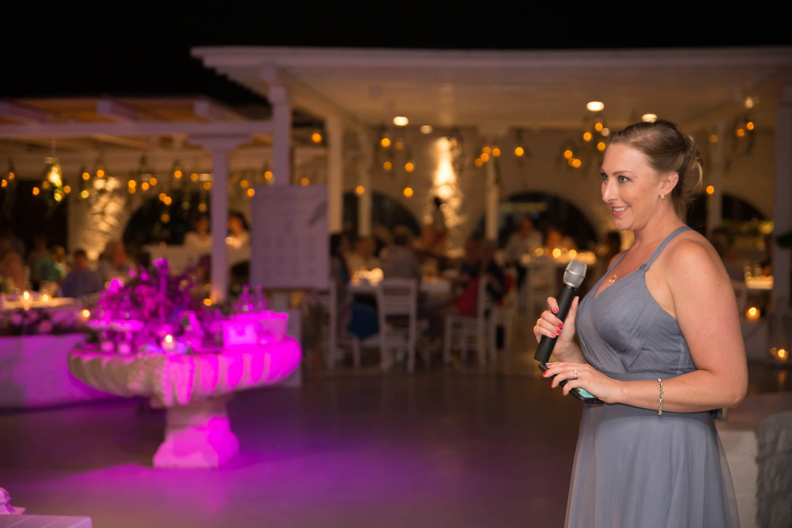 Wedding speech on a wireless microphone, reception tables uplit in magenta