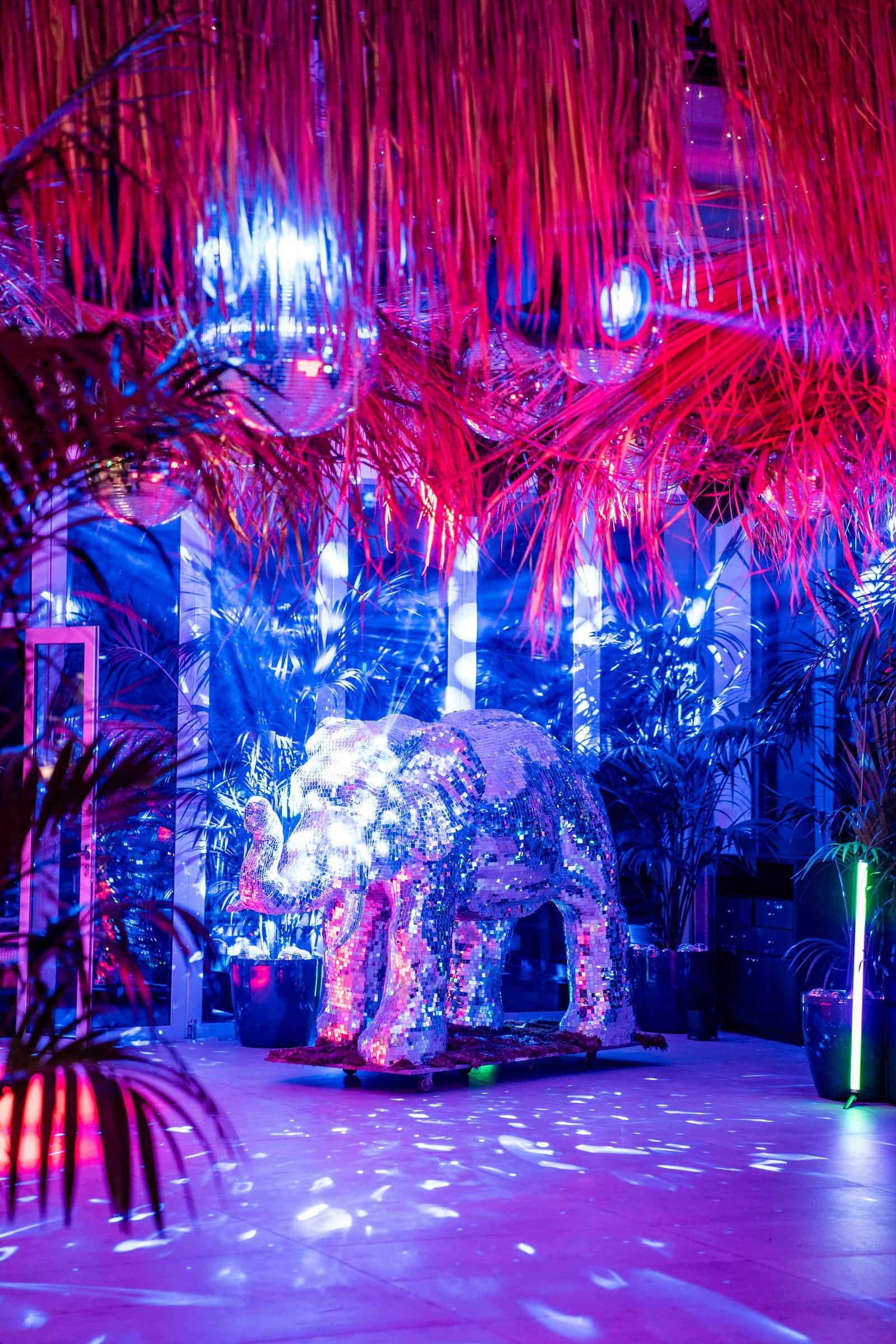 Mirror-ball elephant on a dance floor beneath a red fringe ceiling, lit in blue and pink
