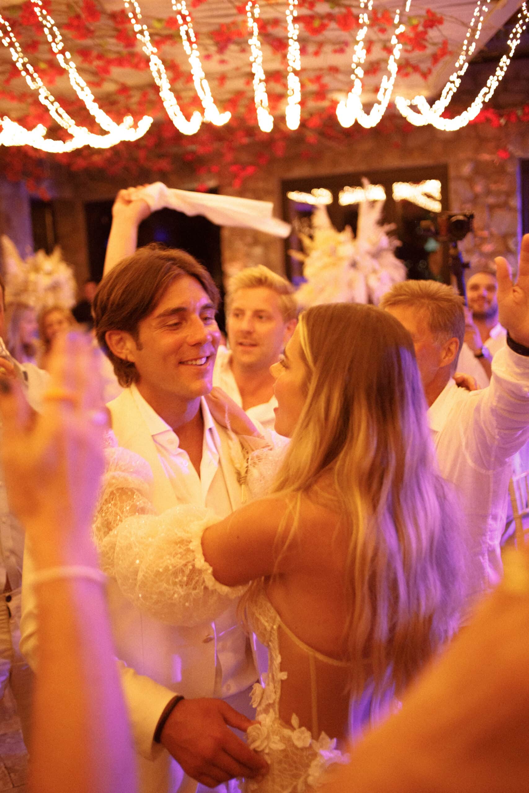 Bride and groom dancing among their guests under warm festoon lights at their Mykonos wedding