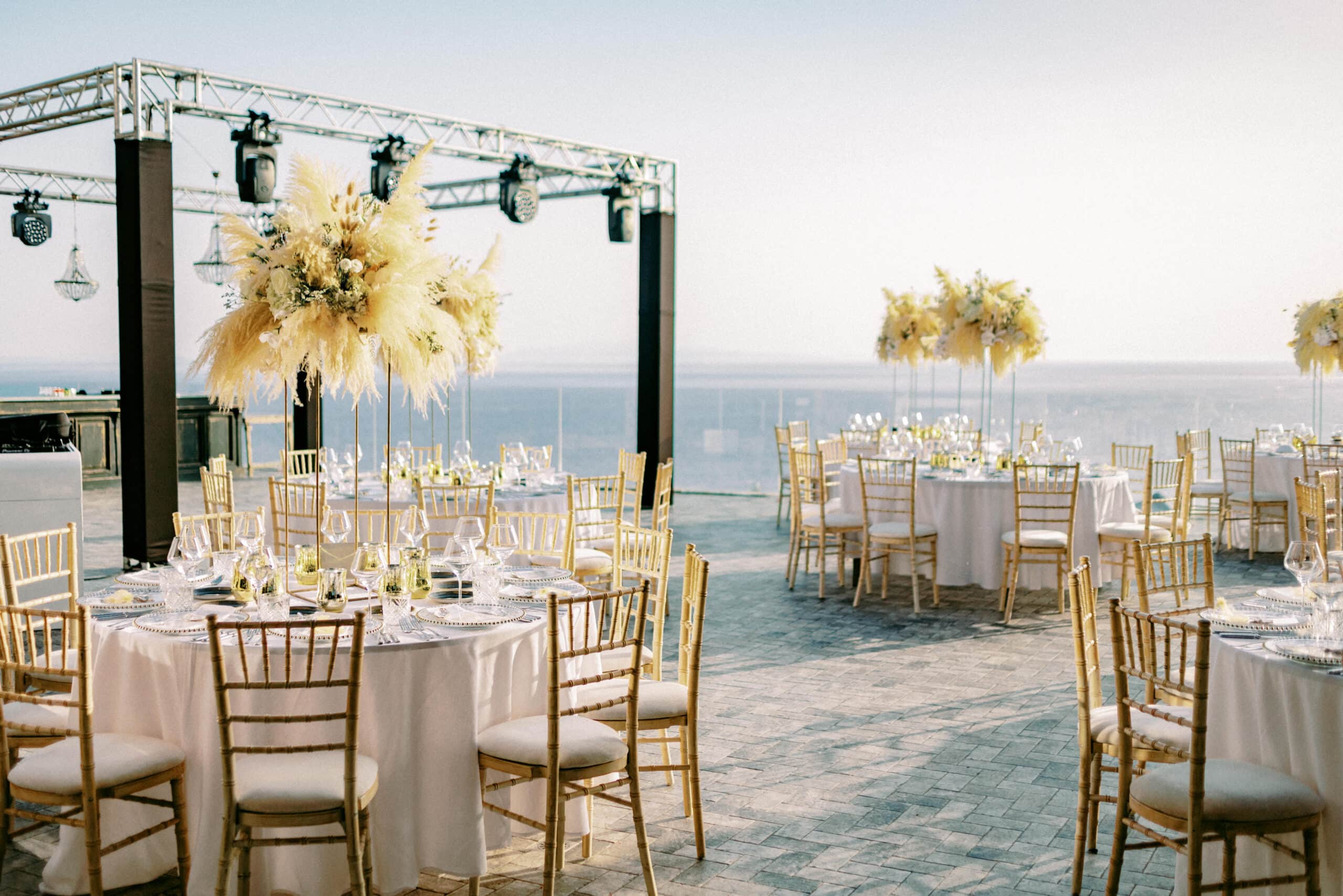 Seaside wedding reception tables framed by a lighting truss with moving heads, Liz and Josh's Mykonos wedding