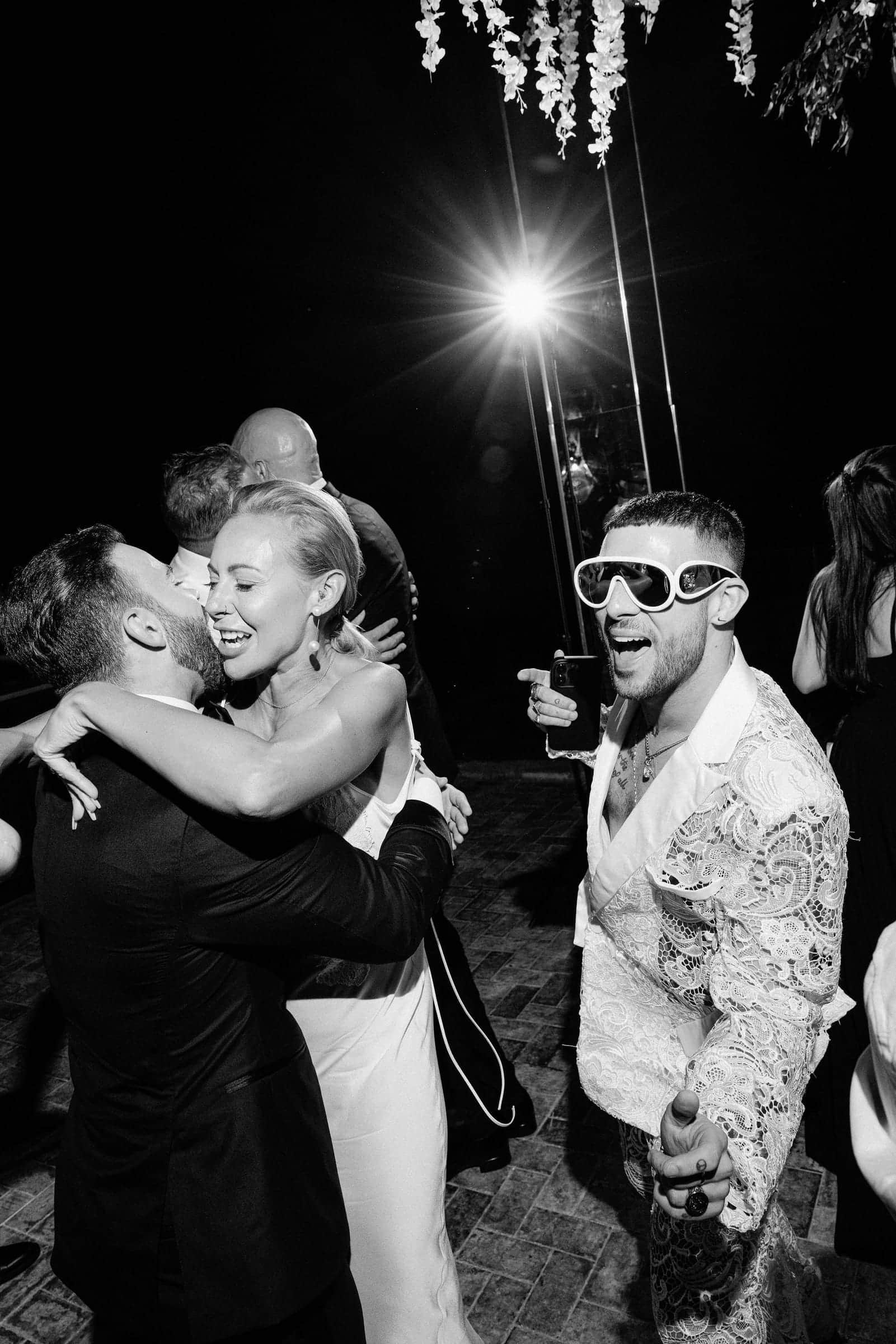 Black-and-white photo of guests embracing and celebrating on a dance floor at night