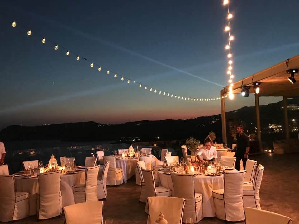 Dinner tables at dusk under festoon string lights, with spotlights rigged on the pergola