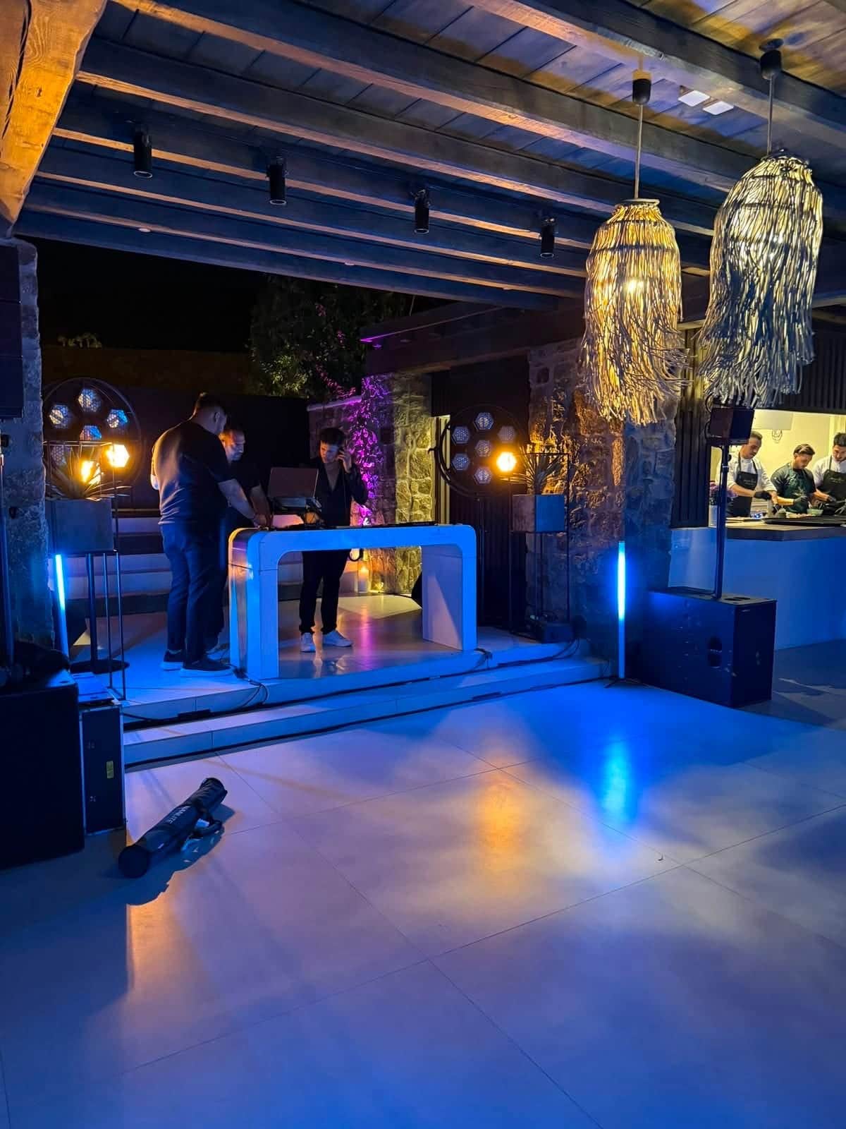 Illuminated DJ booth, speakers and blue uplighting on a covered terrace dance floor before an event